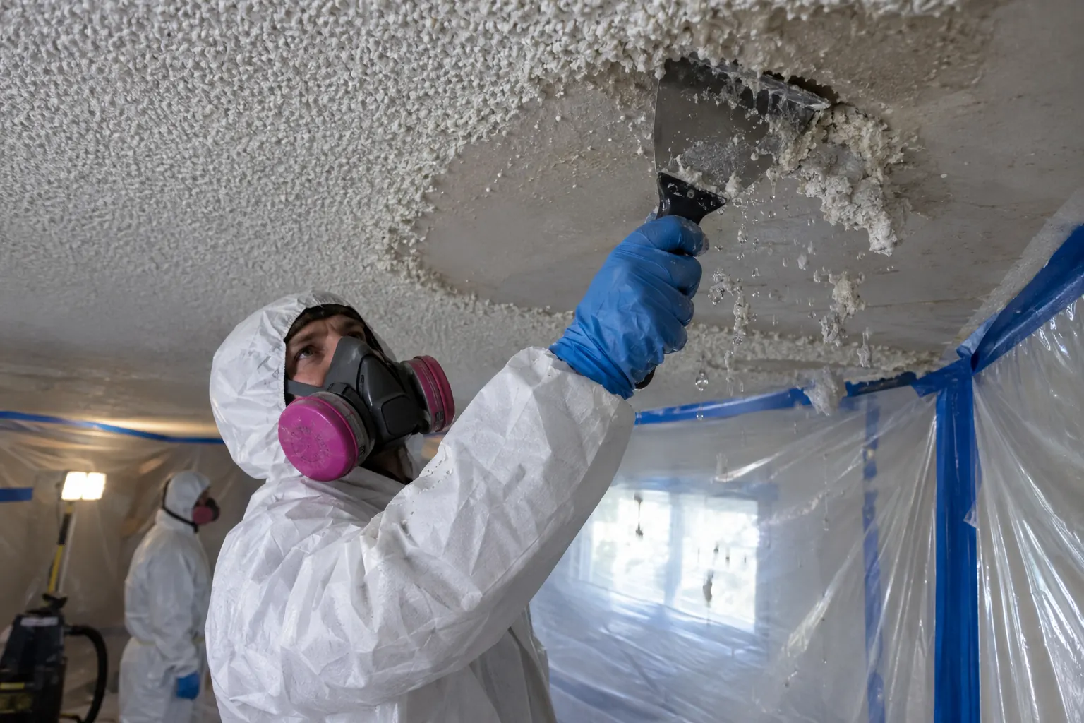 Worker scraping wetted popcorn ceiling texture onto poly sheeting