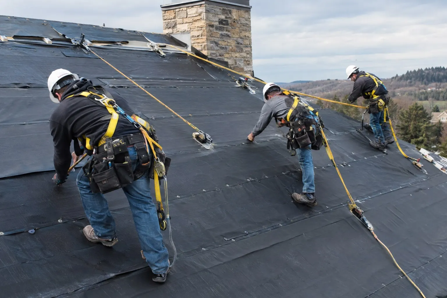Roofing crew tied off with fall protection on a steep residential roof